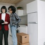 Two women reviewing documents in a kitchen amid moving boxes.